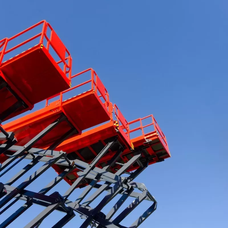 Group of red scissor lifts on a clear blue sky background, low angle perspective shot